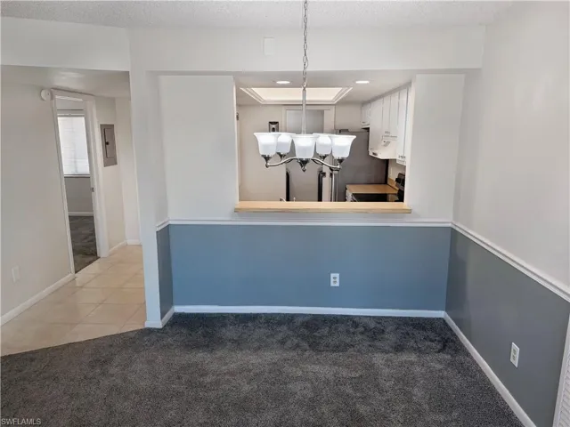 Unfurnished dining area with dark colored carpet, electric panel, suspended lighting, and a textured ceiling