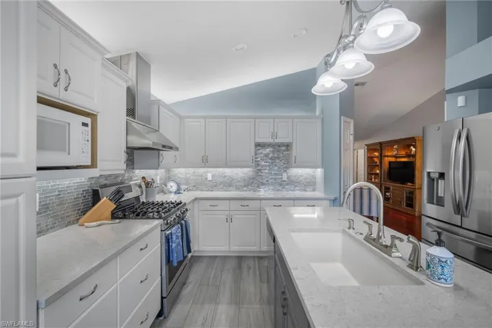 Kitchen with lofted ceiling, white cabinetry, wall chimney range hood, and stainless steel appliances