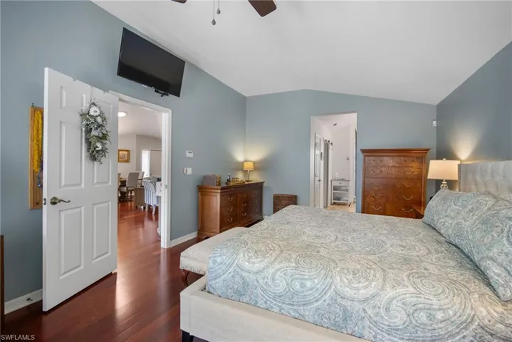 Bedroom featuring ensuite bathroom, vaulted ceiling, dark hardwood / wood-style floors, and ceiling fan