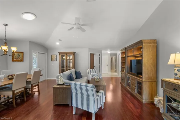 Living room featuring dark wood-type flooring, vaulted ceiling, and ceiling fan with notable chandelier