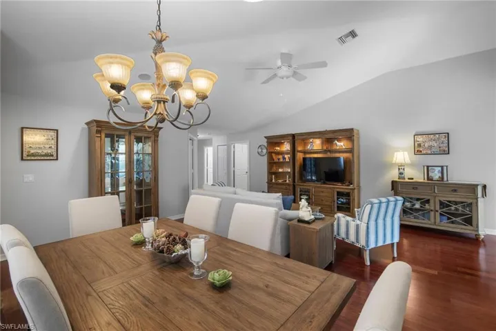 Dining space with vaulted ceiling, ceiling fan with notable chandelier, and dark hardwood / wood-style flooring