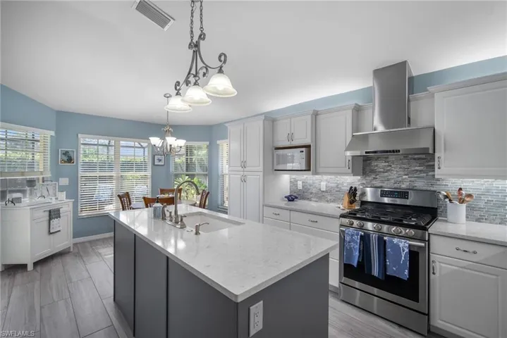 Kitchen with wall chimney exhaust hood, stainless steel gas range, a center island with sink, sink, and white cabinetry