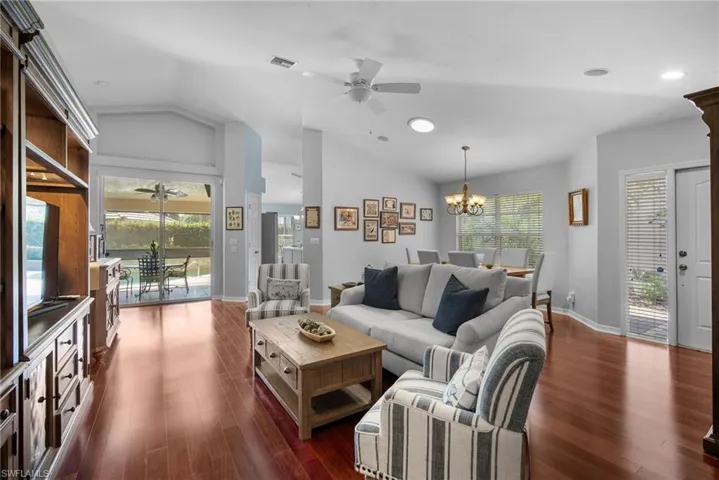 Living room with a wealth of natural light, dark wood-type flooring, vaulted ceiling, and ceiling fan with notable chandelier