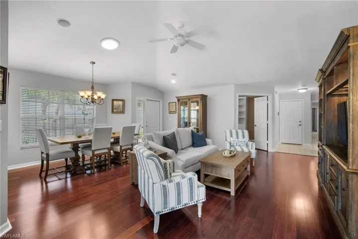 Living room with vaulted ceiling, ceiling fan with notable chandelier, and dark hardwood / wood-style flooring