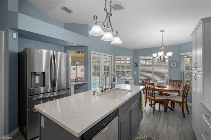 Kitchen with hanging light fixtures, an island with sink, appliances with stainless steel finishes, gray cabinets, and sink