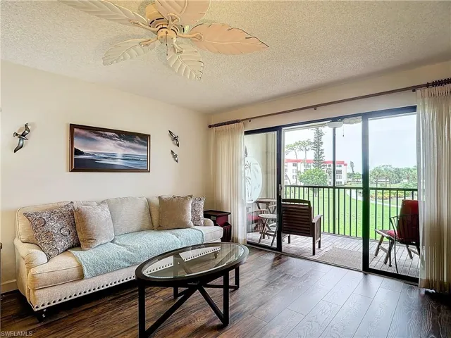 Living room with ceiling fan, dark wood-type flooring, and a textured ceiling
