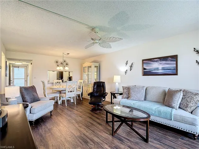 Living room featuring dark hardwood / wood-style floors, ceiling fan with notable chandelier, and a textured ceiling