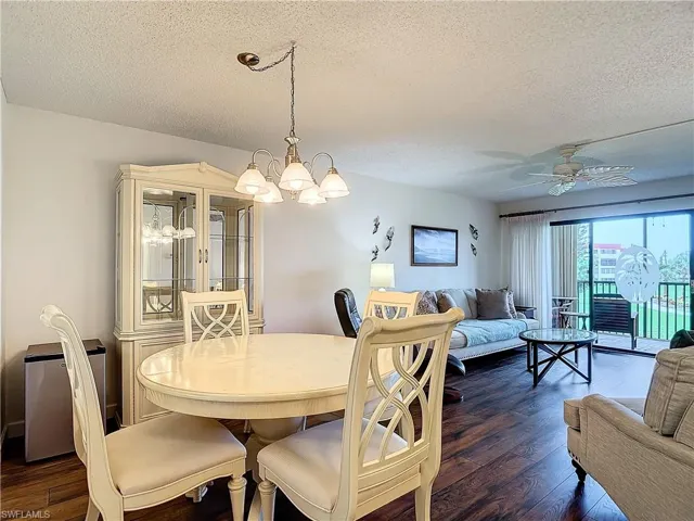 Dining space featuring ceiling fan with notable chandelier, dark wood-type flooring, and a textured ceiling