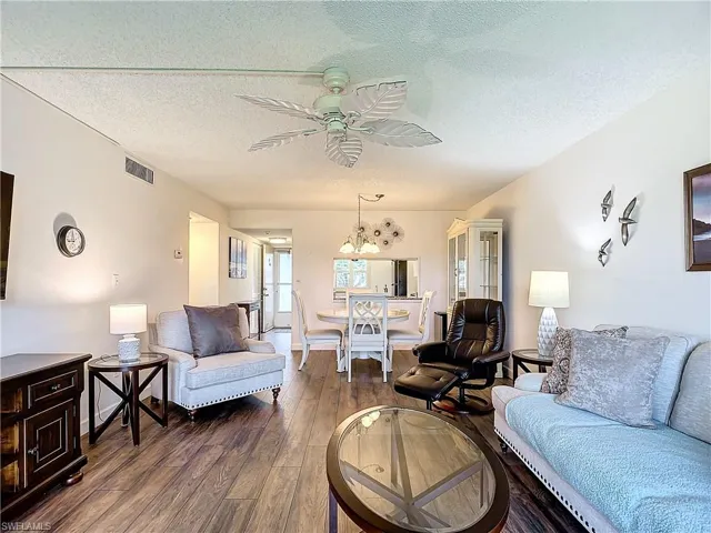 Living room featuring dark hardwood / wood-style floors, ceiling fan with notable chandelier, and a textured ceiling