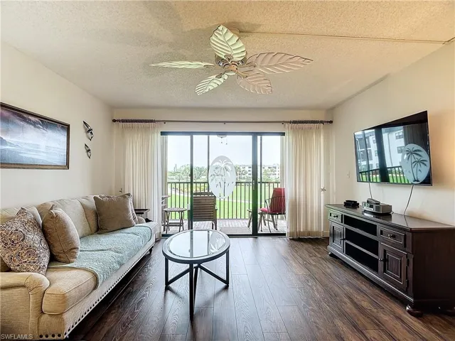 Living room with dark wood-type flooring, ceiling fan, and a textured ceiling