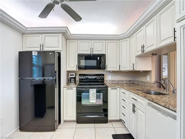 Kitchen featuring sink, light tile patterned floors, stone counters, black appliances, and white cabinets