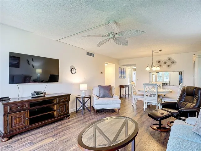 Living room with ceiling fan with notable chandelier, light hardwood / wood-style flooring, and a textured ceiling