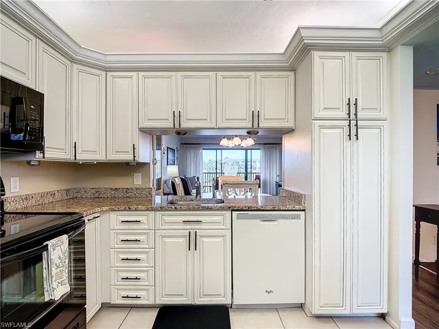 Kitchen featuring sink, light tile patterned floors, kitchen peninsula, stone counters, and black appliances