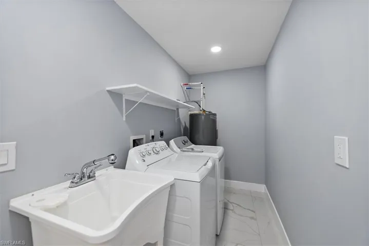 Washroom with light marble finish flooring, electric water heater, washing machine and dryer, baseboards, and recessed lighting