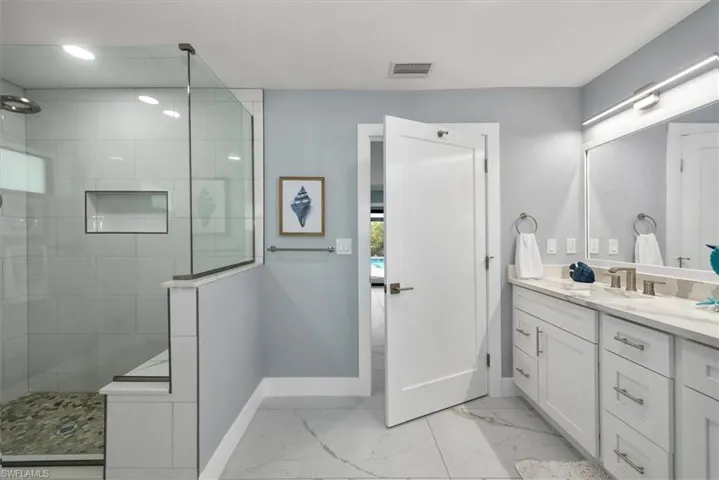 Bathroom featuring baseboards, marble look tiles, a walk in shower, and vanity