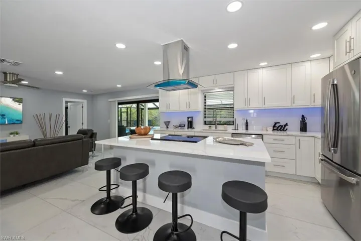 Kitchen with stainless steel appliances, island exhaust hood, open floor plan, a kitchen breakfast bar, and white cabinetry