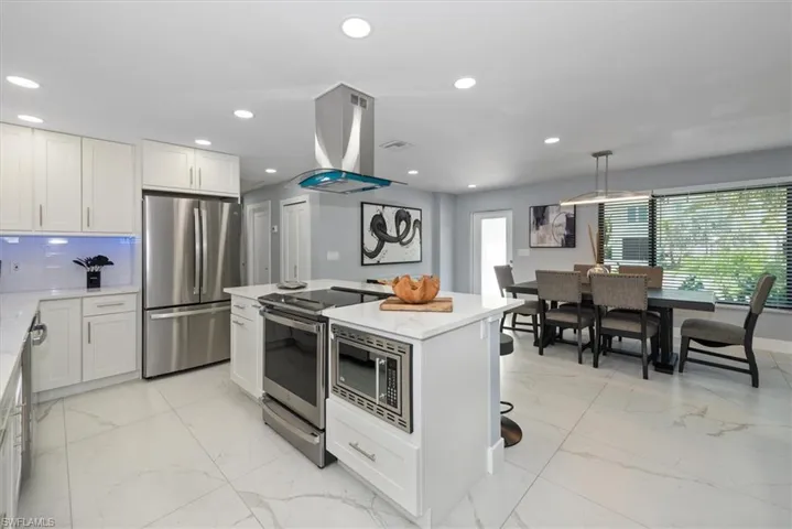 Kitchen featuring stainless steel appliances, island range hood, a center island, light marble finish floors, and white cabinetry