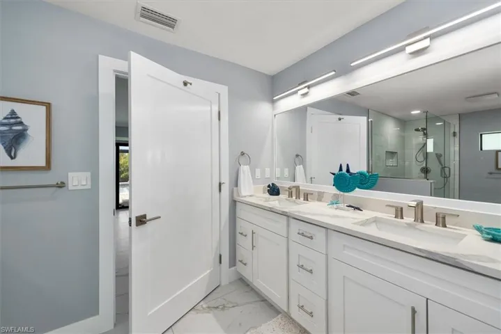 Full bathroom featuring a stall shower, double vanity, marble finish floors, and baseboards