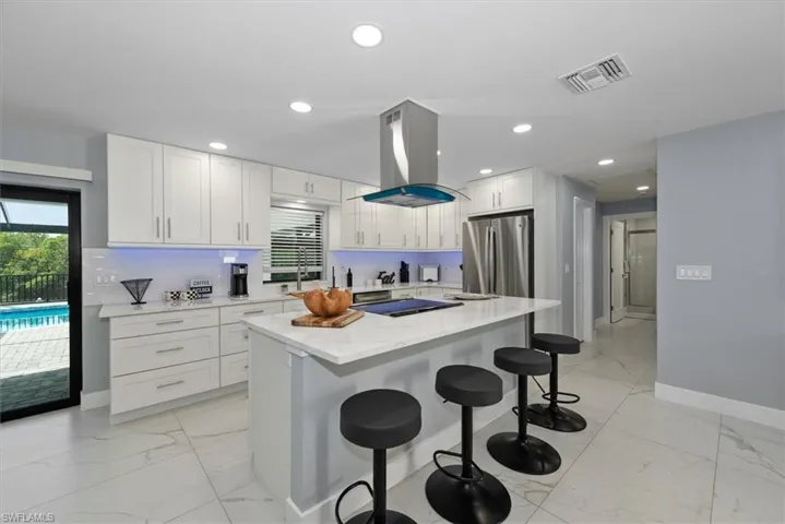 Kitchen featuring freestanding refrigerator, light marble finish flooring, white cabinetry, a kitchen breakfast bar, and recessed lighting