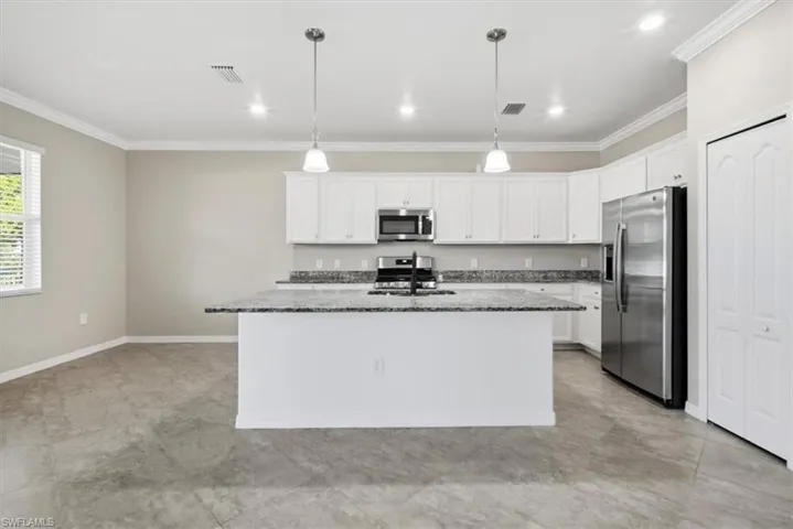 Kitchen featuring appliances with stainless steel finishes, ornamental molding, dark stone countertops, white cabinets, and decorative light fixtures
