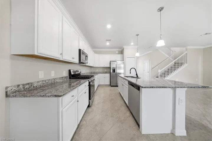 Kitchen featuring stainless steel appliances, hanging light fixtures, white cabinetry, dark stone countertops, and ornamental molding