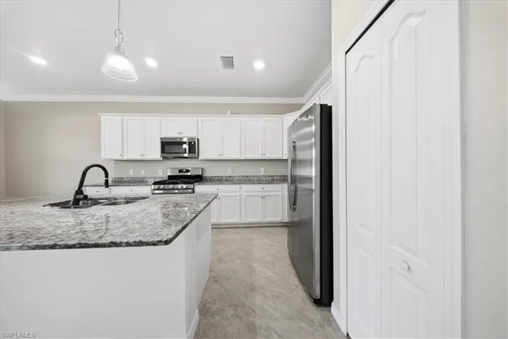 Kitchen with appliances with stainless steel finishes, white cabinetry, ornamental molding, pendant lighting, and light stone countertops