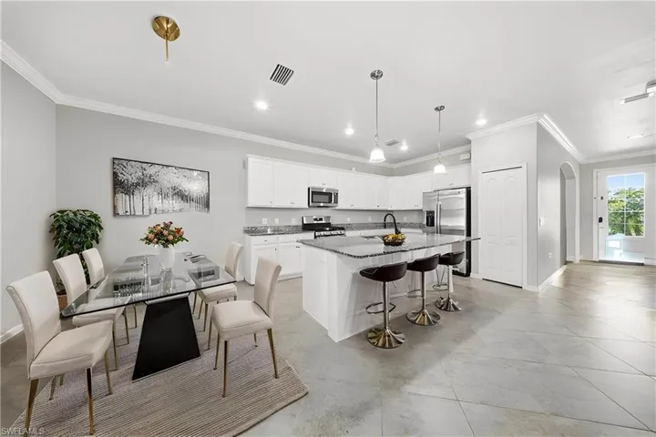 Virtual staging-Kitchen with a breakfast bar area, a kitchen island with sink, appliances with stainless steel finishes, white cabinets, and crown molding
