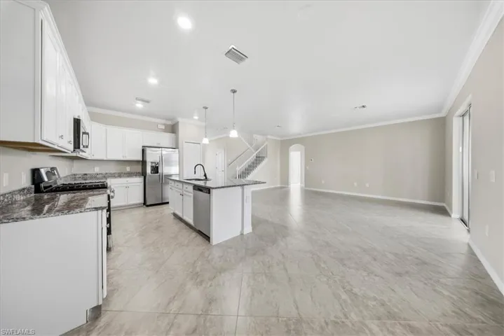 Kitchen featuring decorative light fixtures, stainless steel appliances, ornamental molding, dark stone counters, and white cabinets