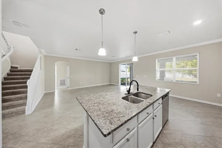 Unfurnished living room featuring arched walkways, crown molding, stairs, and plenty of natural light