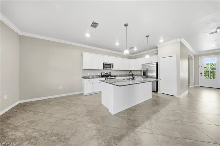 Kitchen featuring crown molding, an island with sink, appliances with stainless steel finishes, arched walkways, and decorative light fixtures