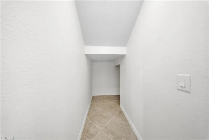 Corridor featuring light tile patterned floors, a textured wall, and lofted ceiling
