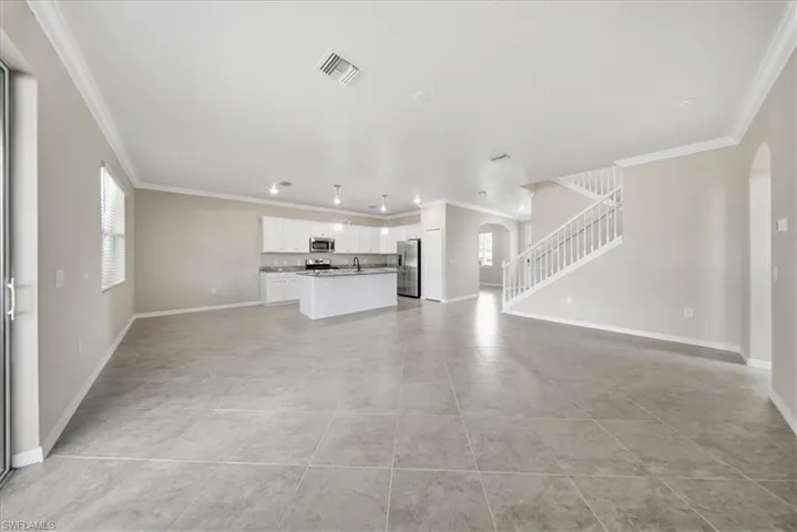 Unfurnished living room featuring arched walkways, crown molding, stairs, and plenty of natural light