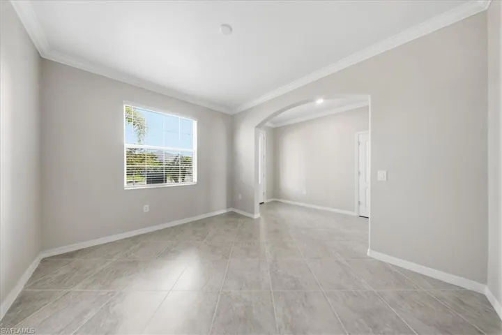 Spare room featuring crown molding, arched walkways, and light tile patterned floors