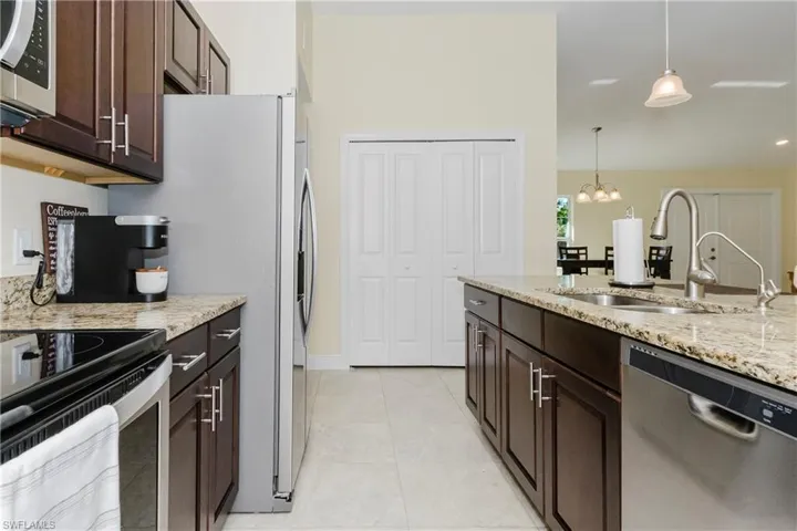 Kitchen with wood cabinets, stainless steel appliances, decorative light fixtures, and light granite counters