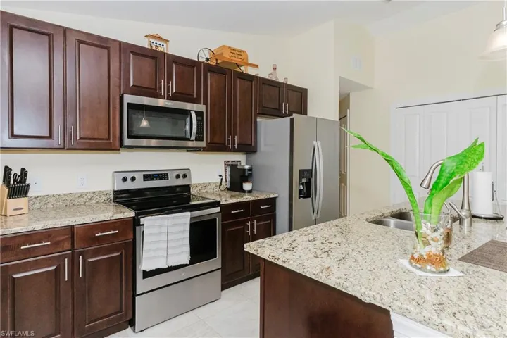 Kitchen with stainless steel appliances, light stone counters, and dark brown cabinetry