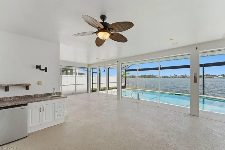 Swimming pool featuring a lanai, a sunroom, a water view, and exterior kitchen