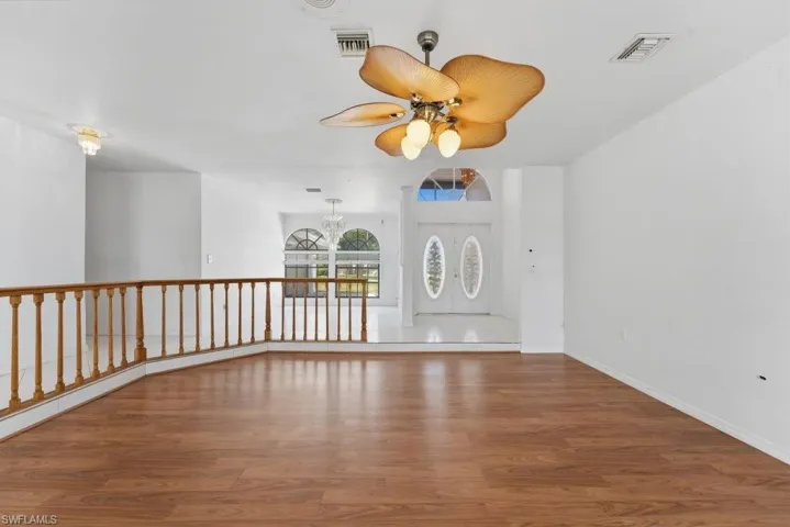 Empty room with ceiling fan, dark wood-type flooring, and suspended lighting