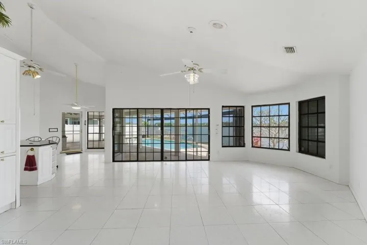 Empty room featuring healthy amount of natural light, lofted ceiling, ceiling fan, and light tile patterned floors