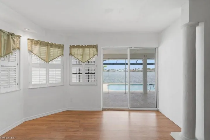 Empty room with light wood-style floors, a water view, and ornate columns