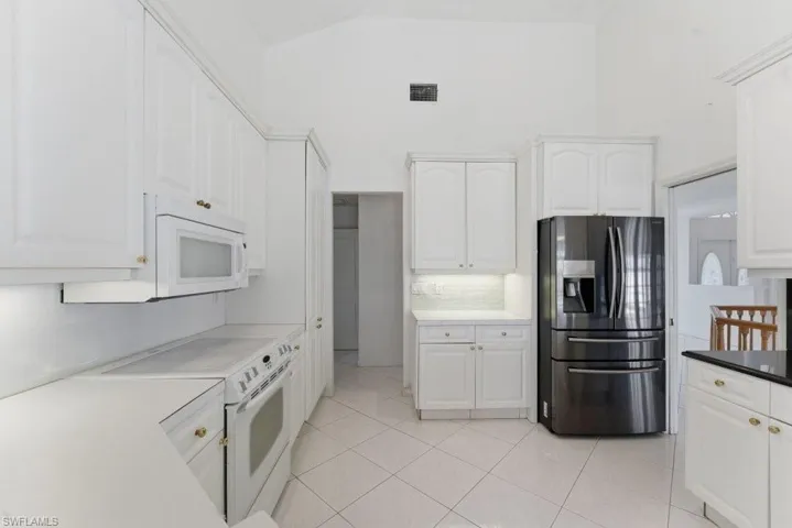 Kitchen featuring white appliances, white cabinetry, light tile patterned floors, lofted ceiling, and light countertops