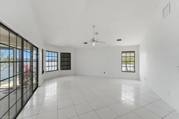 Unfurnished room featuring a ceiling fan, light tile patterned floors, a water view, and lofted ceiling