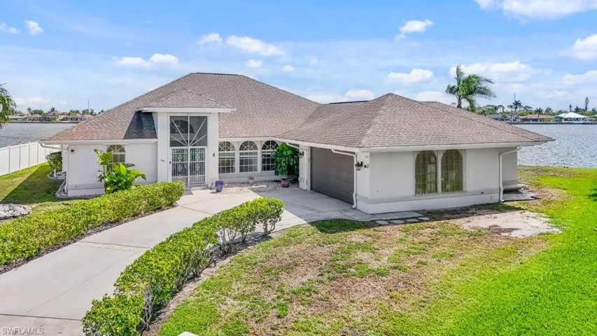 French country style house featuring an attached garage, driveway, a front yard, stucco siding, and a water view