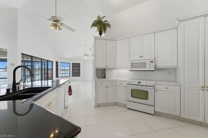 Kitchen with white appliances, white cabinetry, lofted ceiling, a ceiling fan, and light tile patterned floors