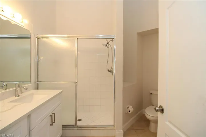 Bathroom featuring walk in shower, tile patterned flooring, vanity, and toilet