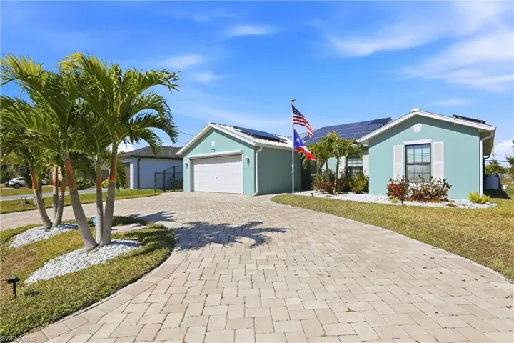 Ranch-style house with curved driveway, stucco siding, solar panels, a front lawn, and a garage