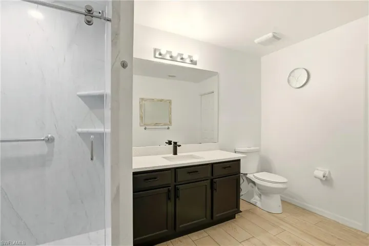 Bathroom featuring a marble finish shower, vanity, and light wood-style flooring
