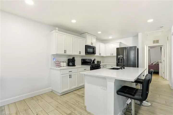 Kitchen with black appliances, a kitchen bar, white cabinetry, wood finish floors, and an island with sink