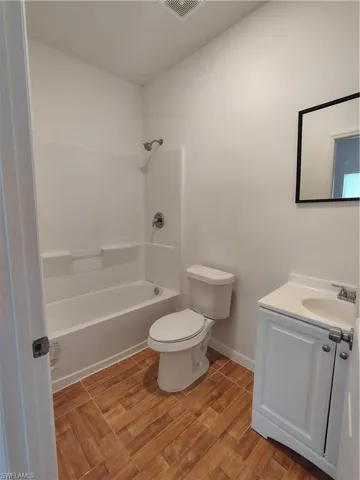 Bathroom featuring a white bathtub/shower combination, a toilet, and a white vanity with an integrated sink
