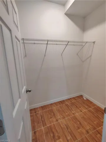 Compact walk-in closet featuring wood-finish tile flooring, white walls, and a wire shelving system