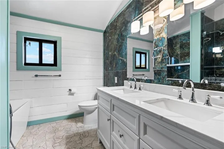 Dual vanity with white cabinetry and integrated sinks, complemented by a large wall mirror and multi-light fixture